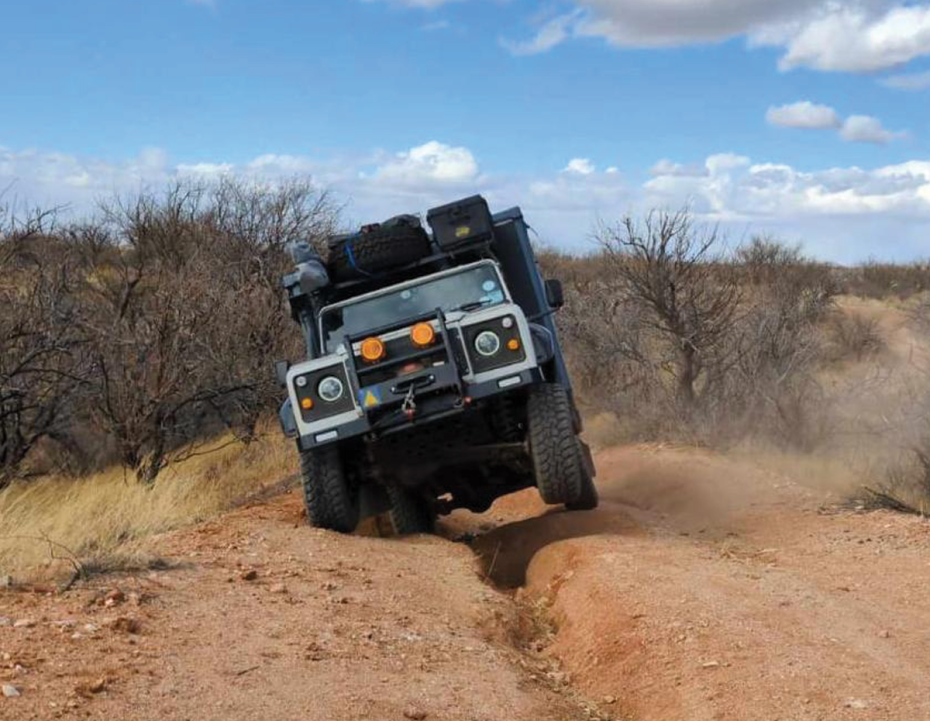 Dramatic sunset with vivid orange and red hues illuminating a textured cloud-filled sky above a silhouette of rugged mountains.